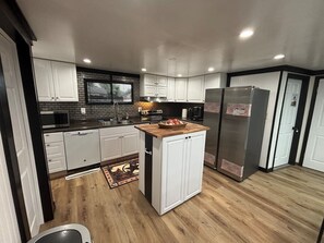 Una cocina moderna con armarios blancos, una isla central, electrodomésticos de acero inoxidable y piso de madera.