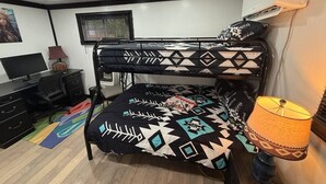 Una cama literera con una colcha estampada, un escritorio con una silla, una lámpara y un televisor.