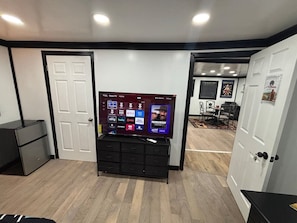 A room with a flat-screen TV on a black stand, a white door, and a wooden floor. - Amazingly located 2 bed 1 bath apart pet friendly (Chattanooga)