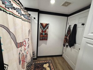 Un pasillo con cortina estampada, alfombra, un tapiz y una puerta con una chaqueta colgada.