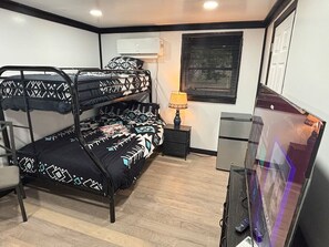 Una habitación con literas, un escritorio, una silla, aire acondicionado, una ventana con persianas y un televisor.
