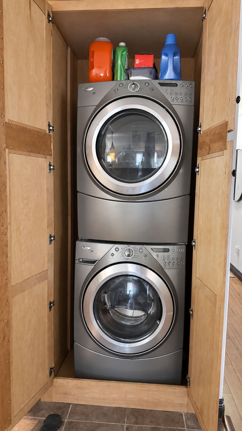 A compact, wooden-framed laundry room with two stacked front-loading washing machines.