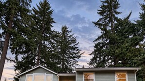 A two-story house with a driveway leading to a garage, surrounded by tall trees. - Peaceful & Spacious Zen Home near Chambers Bay (University Place)