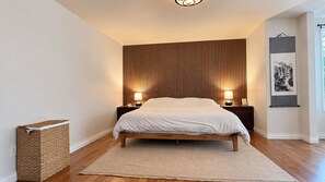 Ein Schlafzimmer mit einem hölzernen Bett, zwei Nachttischlampen, einem gewebten Aufbewahrungsbehälter und einem gerahmten Bild an der Wand.