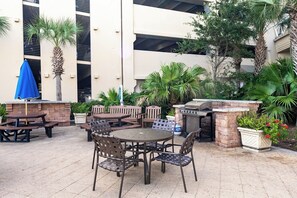 Une terrasse extérieure avec des tables et des chaises, un barbecue et des plantes en pot.