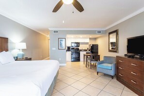 Une chambre d’hôtel comprenant un lit, un bureau, une chaise, une télévision, un ventilateur de plafond et une kitchenette.