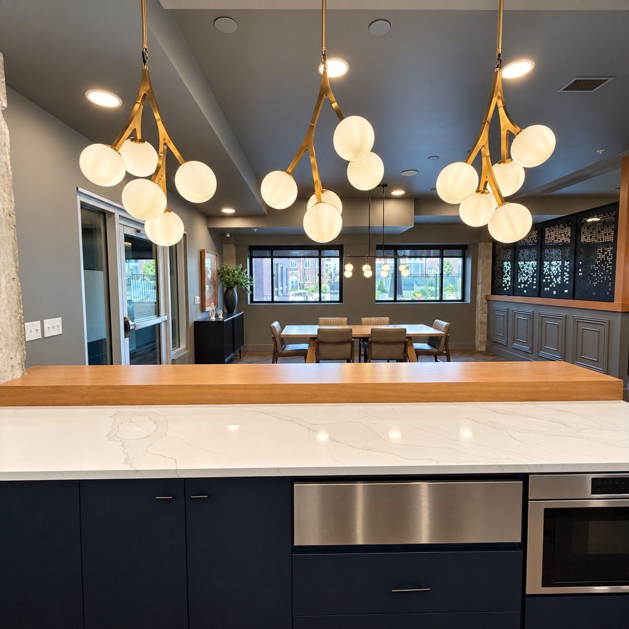 Une cuisine moderne dotée d’un plan de travail en marbre, d’appareils électroménagers en acier inoxydable et d’un luminaire suspendu au design original.