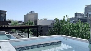 A rooftop swimming pool with clear blue water, surrounded by a wooden deck and modern buildings in the background. - Modern Downtown SLC | King Bed + Free Parking (Salt Lake City)