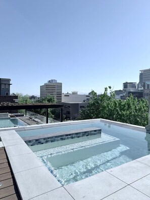 Ein Dachpool mit klarem, blauem Wasser, umgeben von einer Holzterrasse und modernen Gebäuden im Hintergrund.