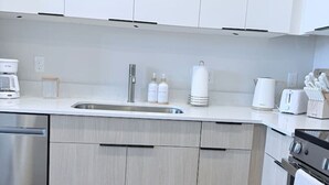 A modern kitchen with white cabinets, stainless steel appliances, and a kitchen mat with the text 'home sweet home' on the floor. - Modern Downtown SLC | King Bed + Free Parking (Salt Lake City)