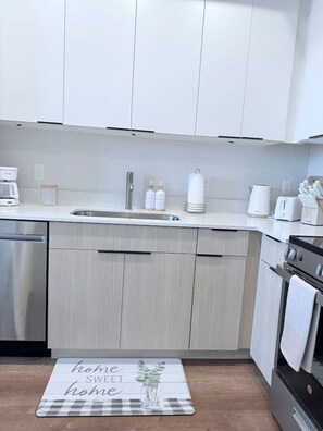 Eine moderne Küche mit weißen Schränken, Edelstahlgeräten und einer Fußmatte mit der Aufschrift 'home sweet home' auf dem Boden.