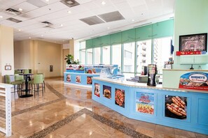 Un bancone gastronomico con un cartello per il gelato Hershey's, un'area con sedute e tavoli, e vista all'esterno attraverso ampie finestre.