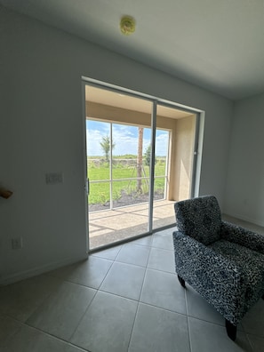 A room with a patterned sofa, a sliding glass door leading to a balcony, and a view of a green landscape. - New 3BR Townhome in Naples - Resort Pools & Gym (Naples)