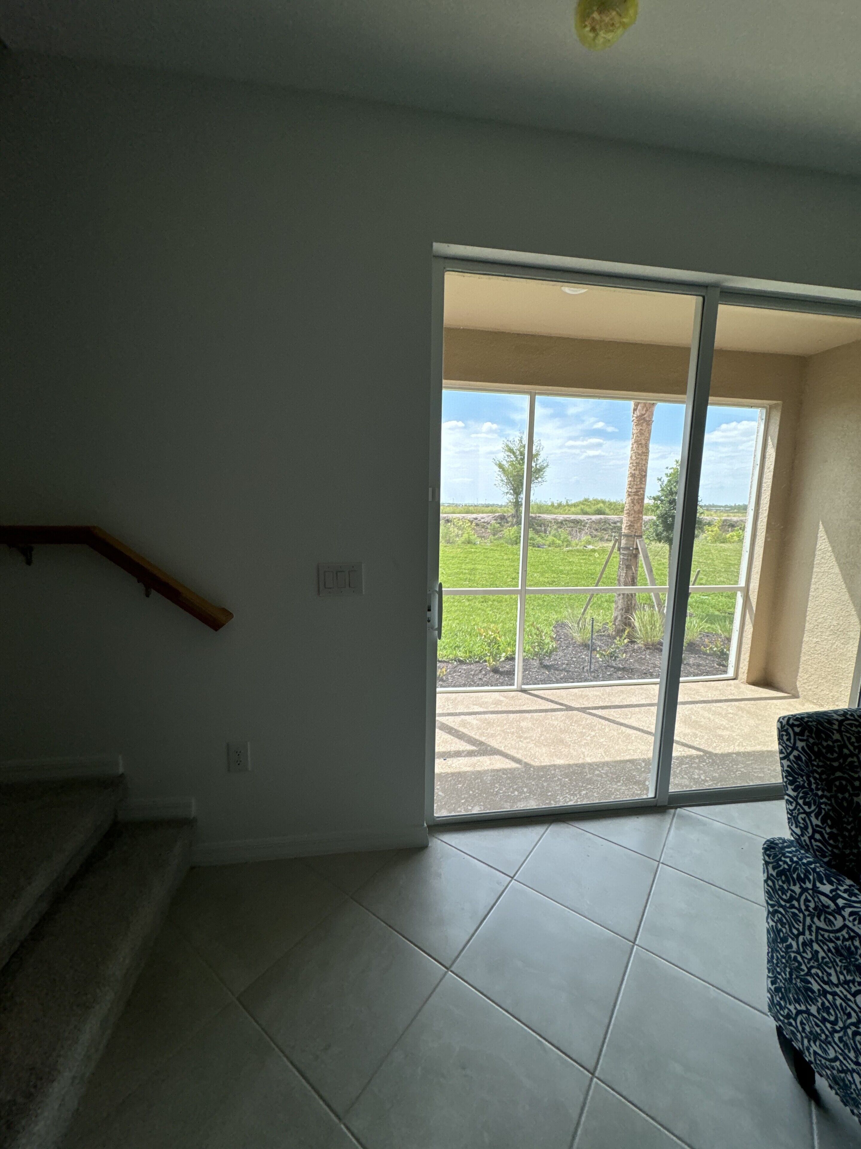 A room with a staircase, a sliding glass door leading to an outdoor area with a view of greenery and a tree.