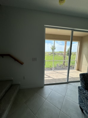 A room with a staircase, a sliding glass door leading to an outdoor area with a view of greenery and a tree. - New 3BR Townhome in Naples - Resort Pools & Gym (Naples)