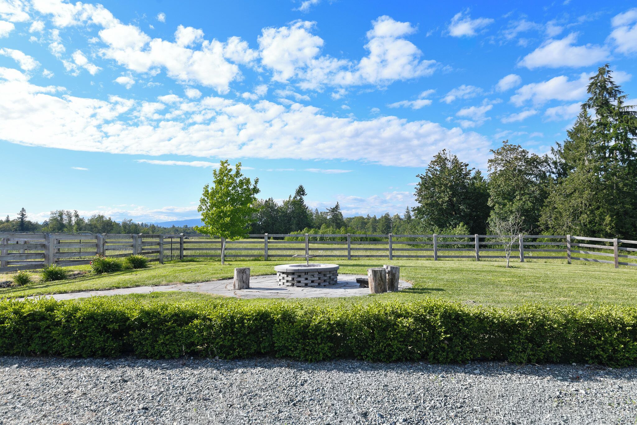 A fenced outdoor area with a circular stone structure, a gravel path, and a wooden fence.
