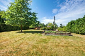 A well-maintained garden with a large tree, a wooden structure, and a clear sky.