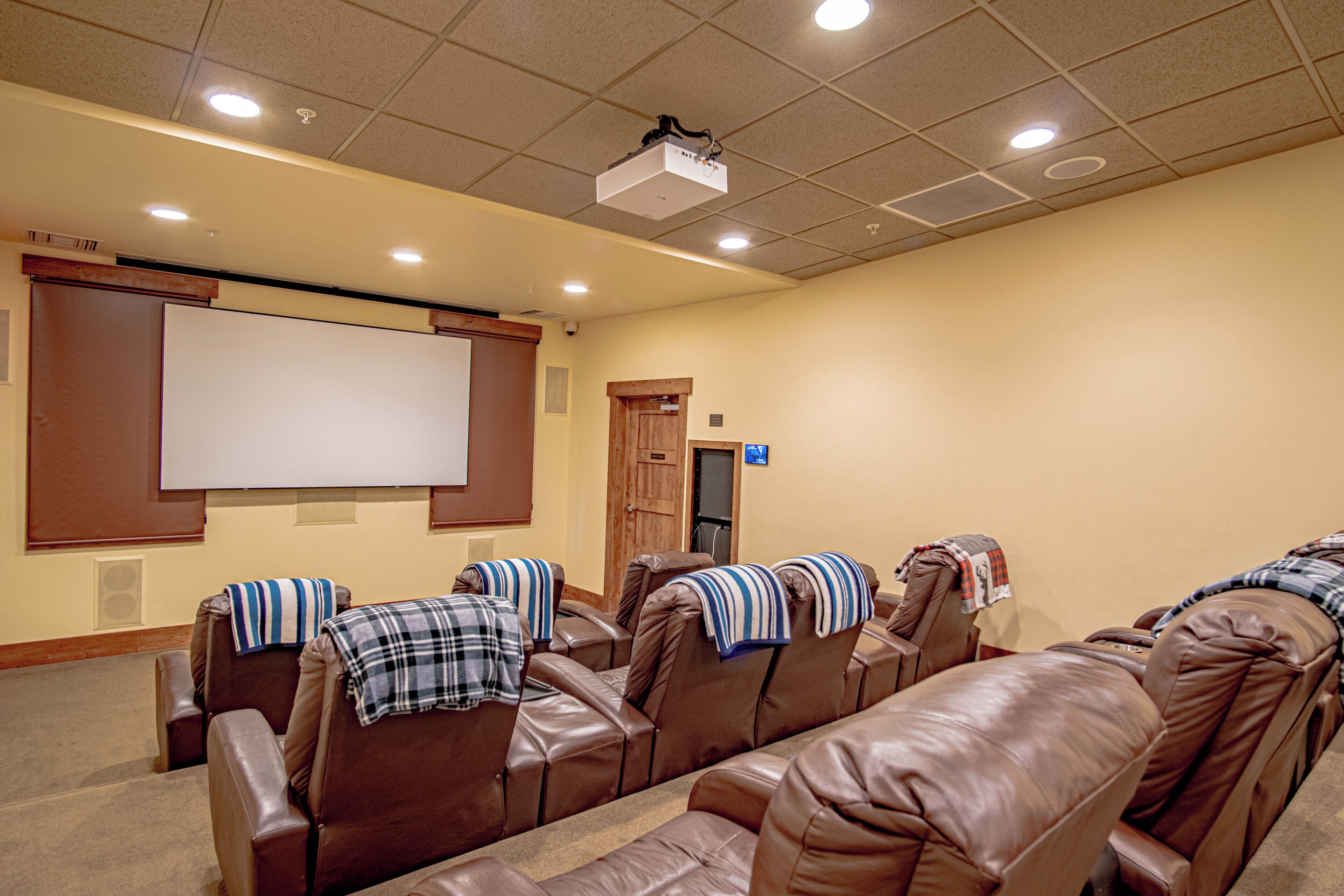 A movie theater with leather reclining seats, a large white screen, and ceiling projectors.