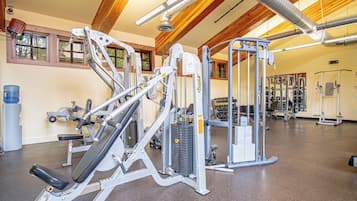 Une salle de sport équipée de divers appareils d’exercice, d’un distributeur d’eau et d’une fenêtre donnant sur des arbres.