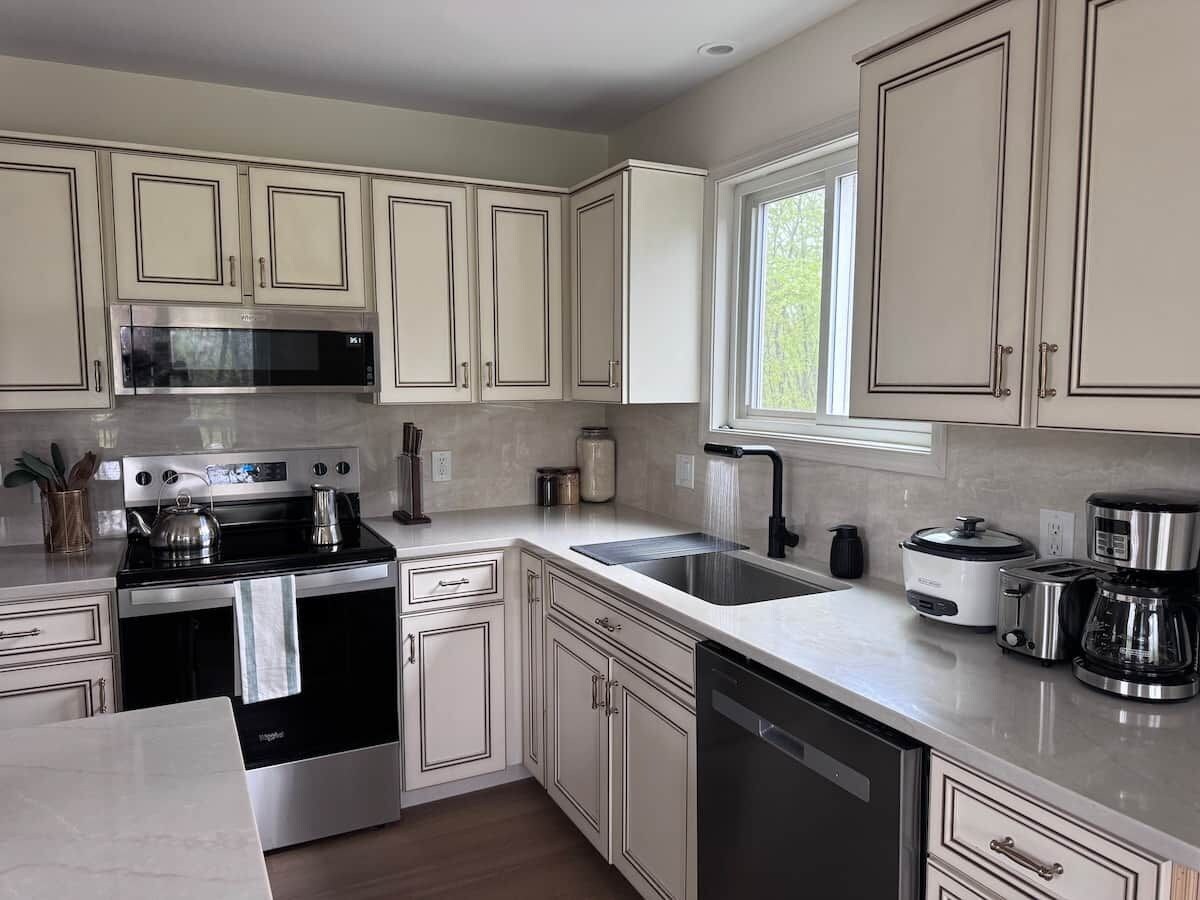 A modern kitchen with stainless steel appliances, white cabinetry, and a window providing natural light.