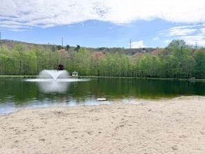 A lake with a fountain in the center, surrounded by trees and a sandy shore. - The Totteridge (Saw Creek)