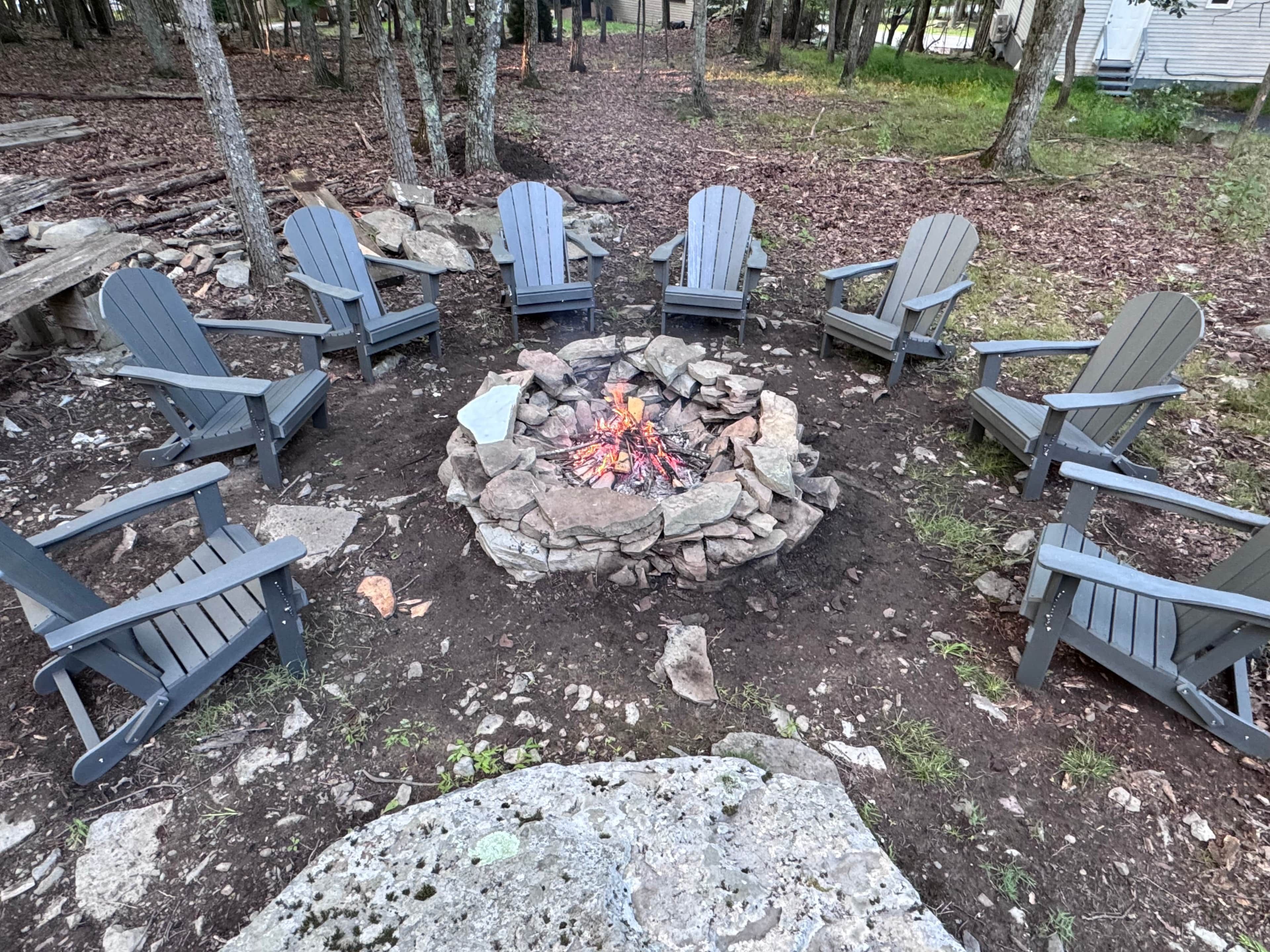 A circular seating arrangement around a central fire pit with rocks, surrounded by trees.