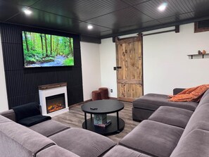 A modern living room with a fireplace, a large flat-screen TV, and a cozy seating area. - The Totteridge (Saw Creek)