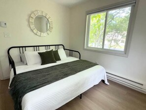 A bedroom with a bed, a round mirror, a window, and a thermostat. - The Totteridge (Saw Creek)