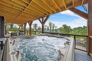 Ein Whirlpool mit Holzterrasse und Sitzgelegenheiten mit Blick auf eine bewaldete Landschaft.