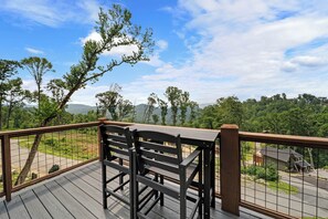 Eine Holzterrasse mit Metallgeländer, die einen üppigen Ausblick auf Bäume und ferne Berge bietet.