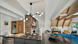 Eine moderne Küche mit Kochinsel, Kamin aus Stein und Essbereich mit Sofa und Fernseher.