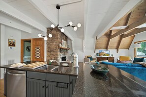 Eine moderne Küche mit Kochinsel, Kamin aus Stein und Essbereich mit Sofa und Fernseher.