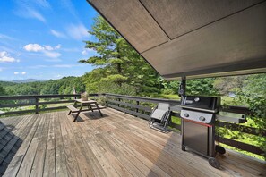 Eine Holzterrasse mit Grill und Picknicktisch, mit Blick auf einen bewaldeten Bereich.