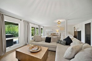 Een ruime woonkamer met een grote bank, een salontafel, en een eethoek met een tafel en stoelen.
