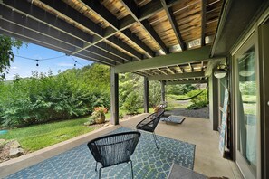 Un porche cubierto al aire libre con una pérgola, dos sillas y vistas a un jardín.