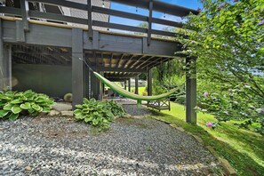 A covered outdoor area with a hammock, potted plants, and a view of a building with a wooden deck. - Private Mountain Getaway Near Boone with Hot Tub (Vilas)