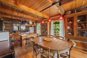 Ein Holzinterieur mit einem zentralen Esstisch, Stühlen, hängenden Töpfen und einer Küchenzeile mit Schränken und einem Kühlschrank.