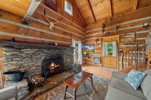 A log cabin interior with a stone fireplace, wooden walls, a sofa, and a television. - Secluded Mountain Escape with Incredible Views (Banner Elk)