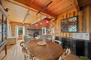 A wooden interior with a round dining table, chairs, a stone fireplace, and a television. - Secluded Mountain Escape with Incredible Views (Banner Elk)