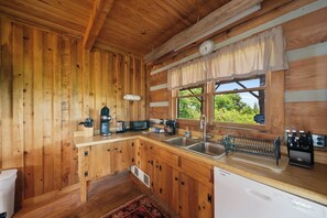 Eine Holzhütte mit einer Küche, inklusive Spüle, Kaffeemaschine, Toaster und einem Fenster mit Vorhängen.