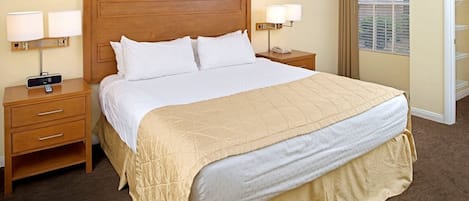 A hotel room with a large bed, two bedside tables with lamps, a nightstand with a phone, and a window with blinds.