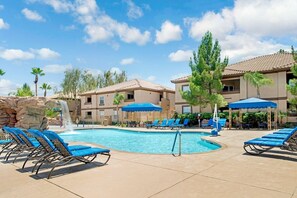 A pool area with lounge chairs, a water feature, and a building with a tiled roof.