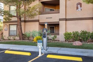 Un edificio con estación de carga para autos eléctricos, un árbol y cielo despejado.