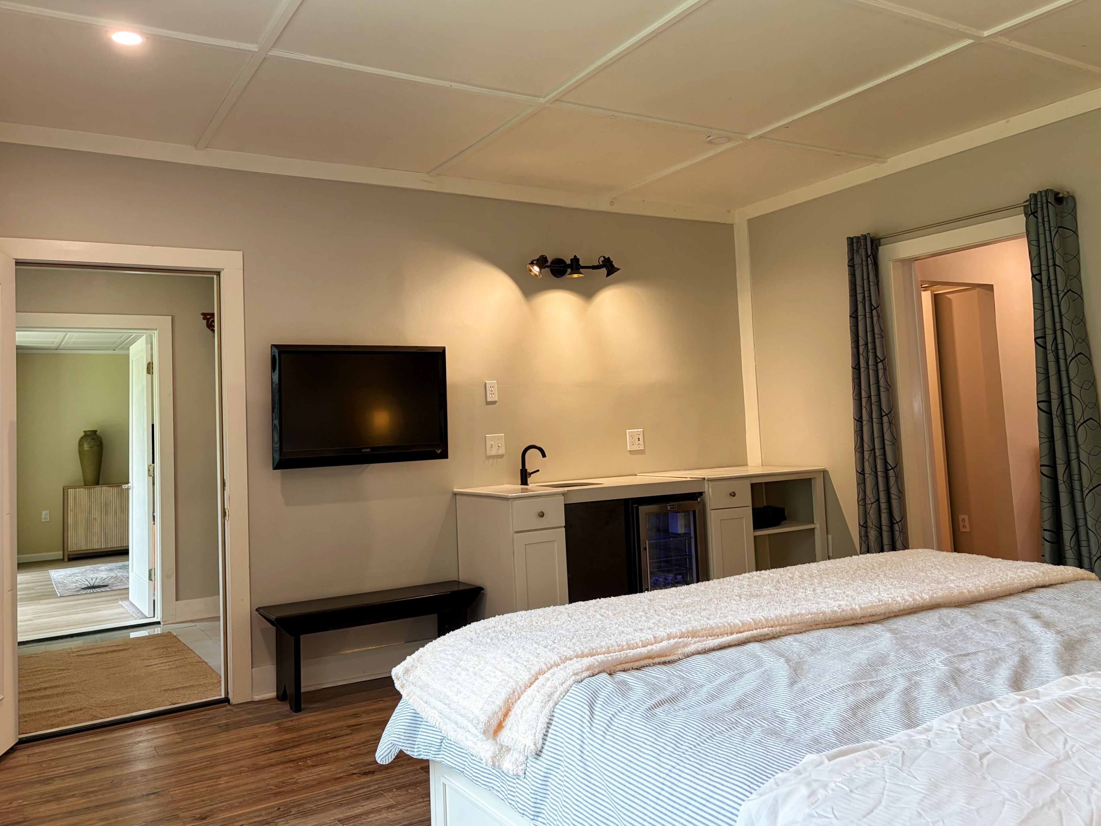 Ett hotellrum med en säng, en bänk, en tv, ett handfat och en dörr.