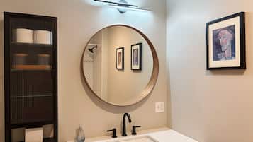 A bathroom with a round mirror, a sink, a towel rack, and a framed picture on the wall.