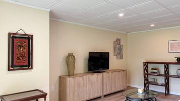 Een woonkamer met een televisie, een kast, een glazen salontafel en een lijst met een afbeelding aan de muur.