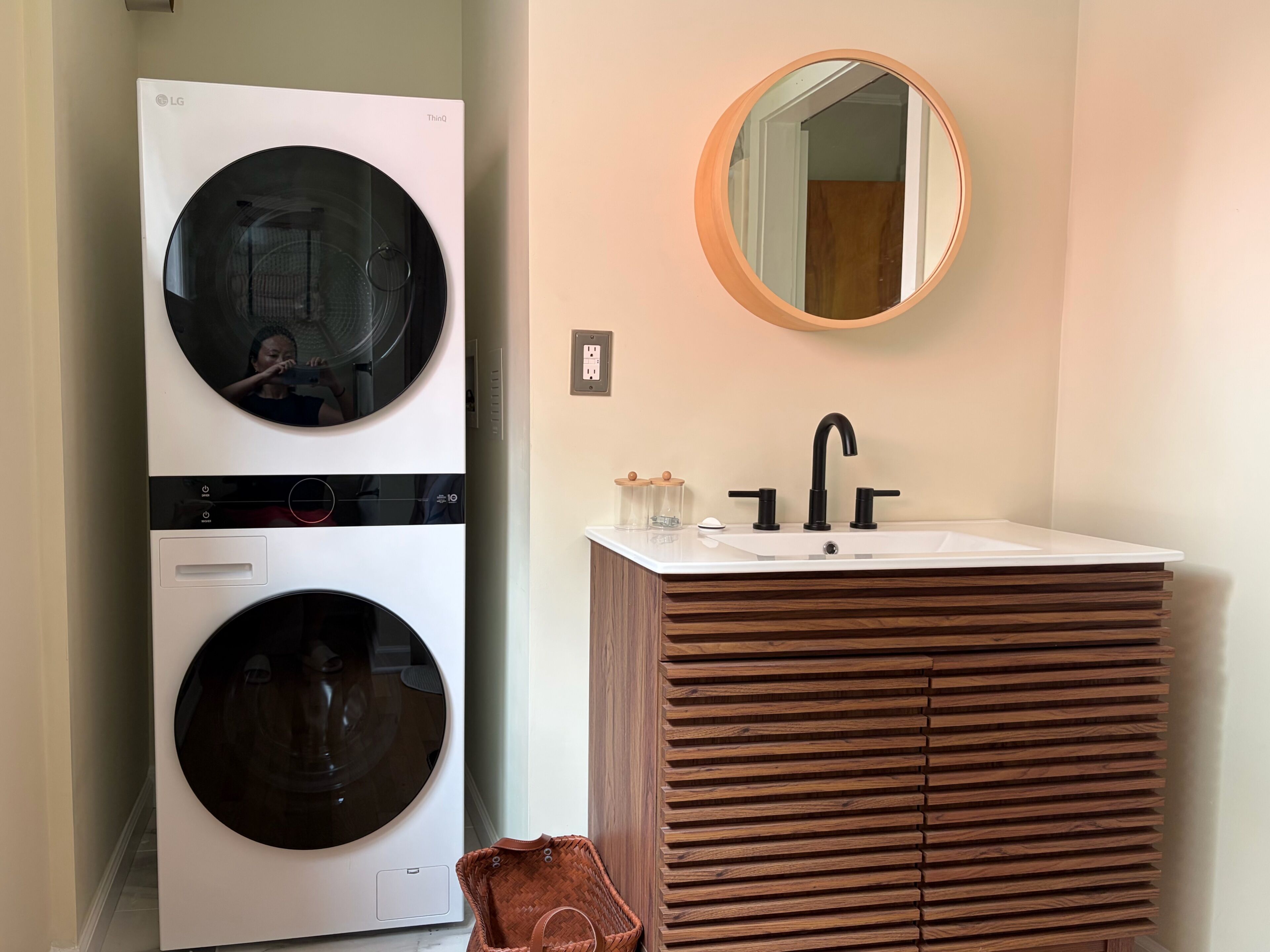 Une buanderie équipée de deux machines à laver superposées et d’un évier avec un meuble-lavabo en bois.