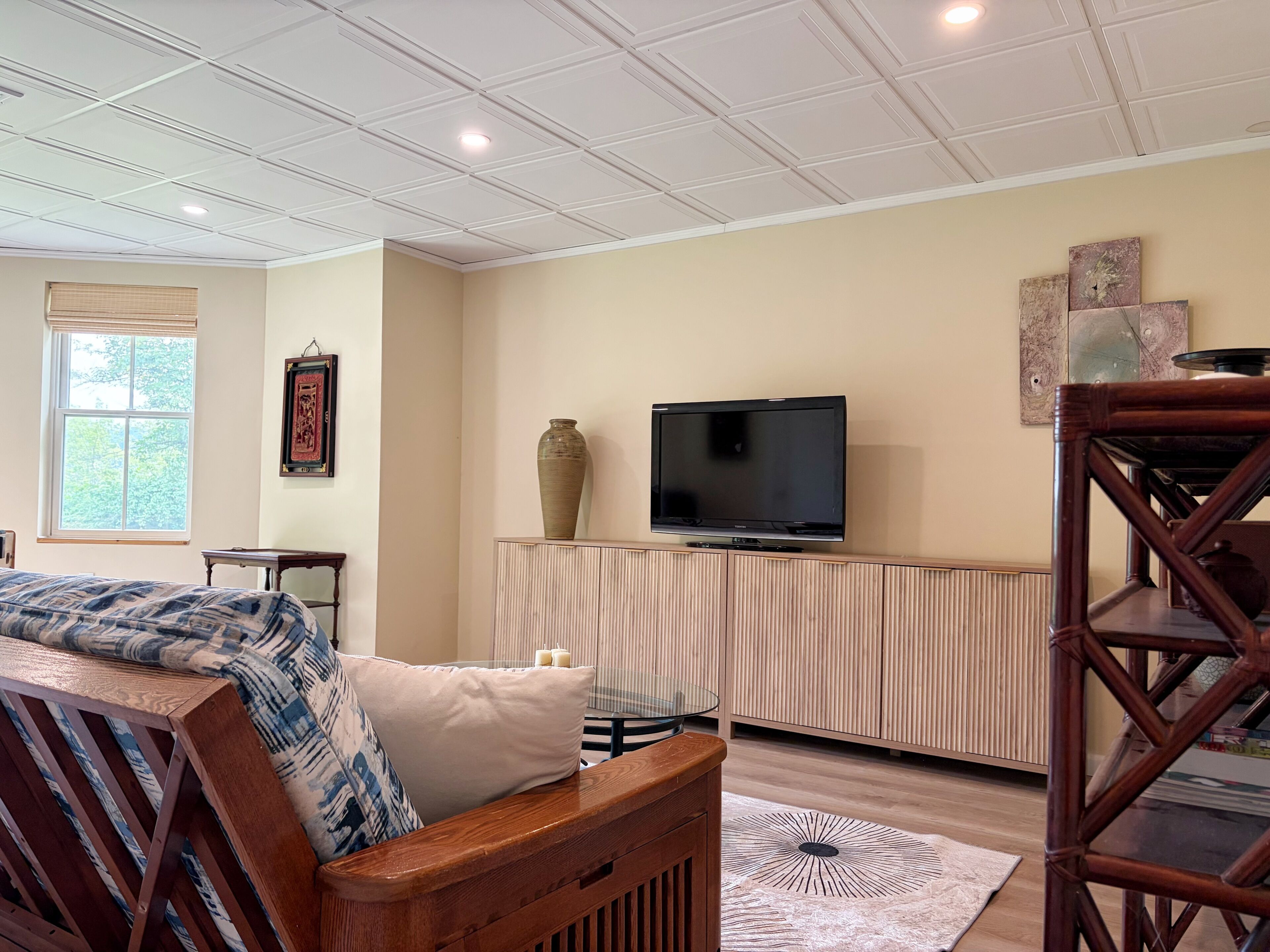 Una sala de estar con una televisión sobre un mueble de madera, una alfombra estampada y una ventana con persianas.
