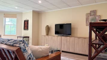 Una sala de estar con una televisión sobre un mueble de madera, una alfombra estampada y una ventana con persianas.
