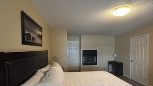 A hotel room with a large bed, a framed picture on the wall, a ceiling light, and a door. - Seaside Cedar Escape (Nanoose Bay)